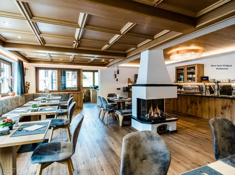Hotelrestaurant mit gedeckten Tischen und einem weißen, freistehenden Kaminofen in der Raummitte