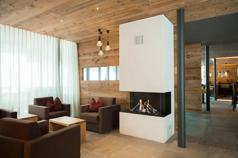 Lounge mit Sesseln und Eckkamin vor einer Altholzwand