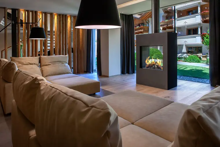 Moderner Wohnraum mit doppelseitigem Kamin als Raumteiler, Blick durch die Glasfront in den Garten