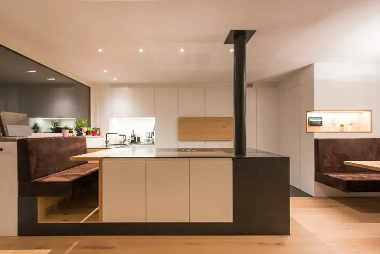 Kochinsel mit Holzherd, angesetzter Sitzbank und massivem Holztisch