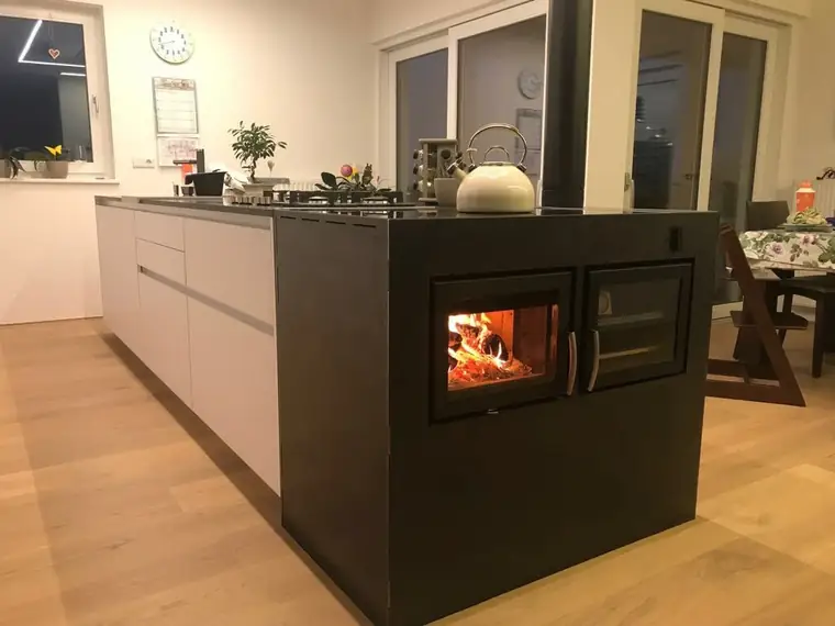 Kochinsel mit brennendem Holzherd neben Gaskochfeld und Essplatz