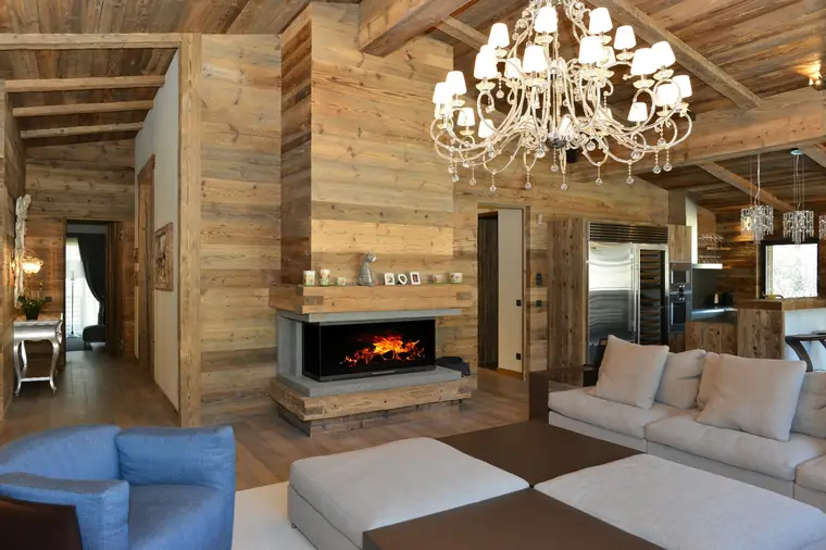 Chalet-Wohnraum mit breitem Kamin unter einer Altholzdecke