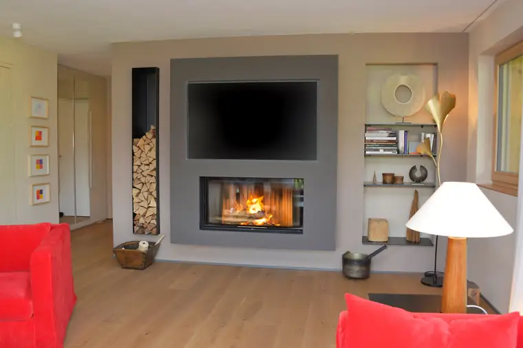 Grauer Kaminblock mit Fernseher und seitlichen Holznischen