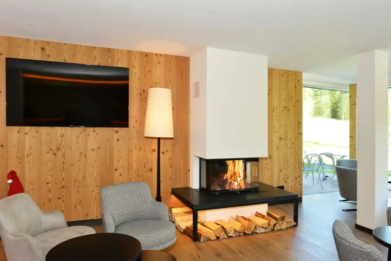 Kamin in einer Holzwand unter einem Fernseher, daneben ein offenes Holzfach