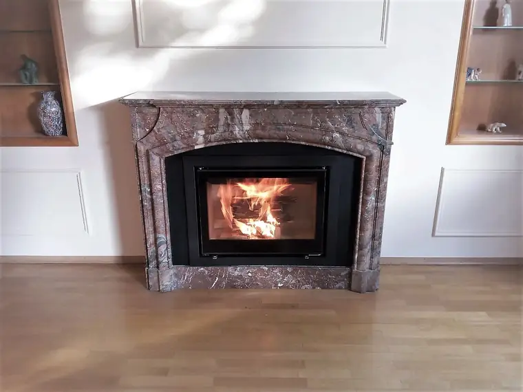 Kamin in einem alten Marmorrahmen vor heller Wand