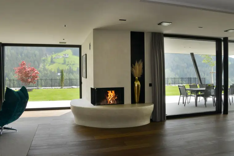 Geschwungene Sitzbank an einem Wandkamin, dahinter der Blick in ein grünes Tal