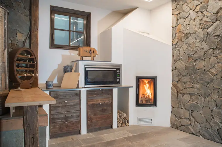Kamin in einer Natursteinwand neben Altholzmöbeln