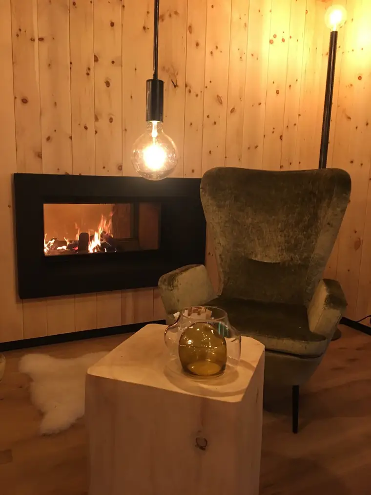 Breiter Kamin in einer Zirbenwand, davor ein Ohrensessel