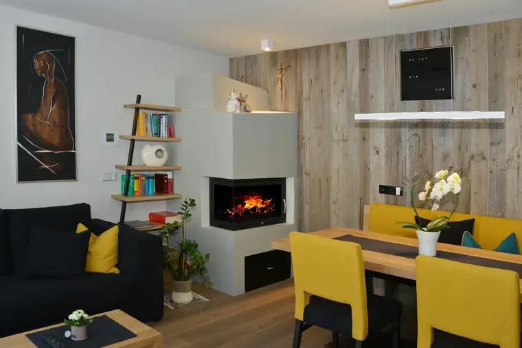 Kamin an einer Altholzwand, davor gelbe Stühle