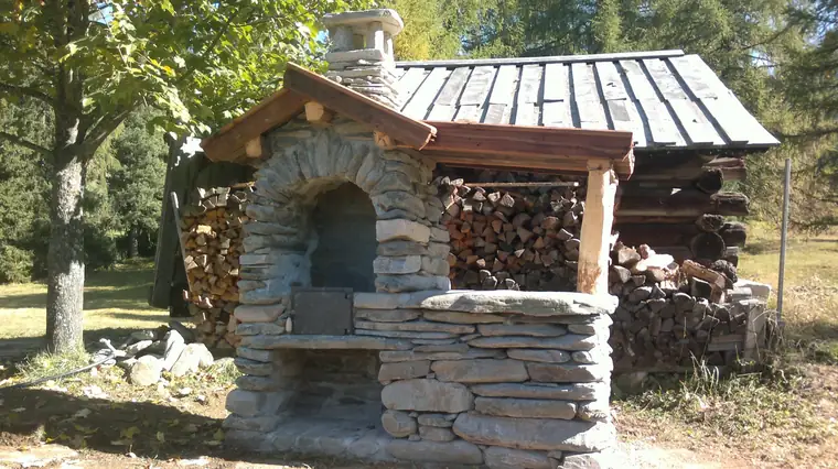 Steinbackofen mit Schindeldach und aufgeschichtetem Brennholz