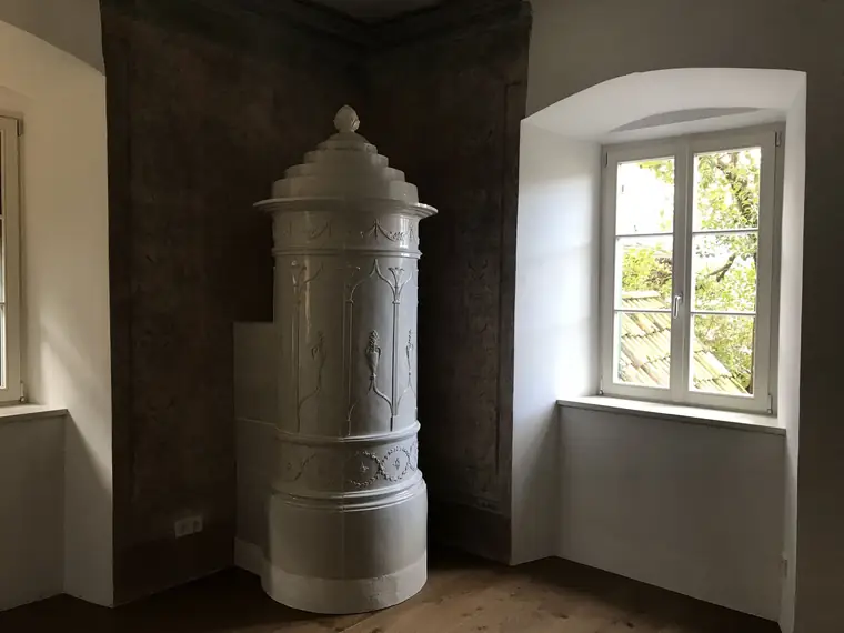 Grauer historischer Ofen an einem tiefen Fenster
