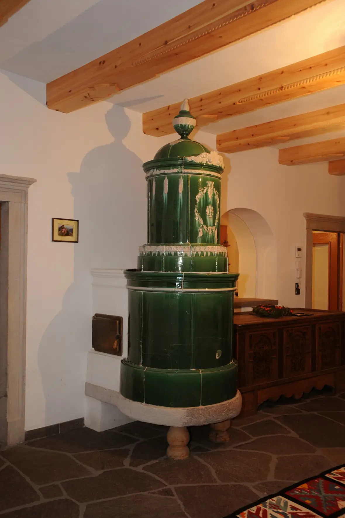 Grüner historischer Säulenofen unter einer Holzdecke