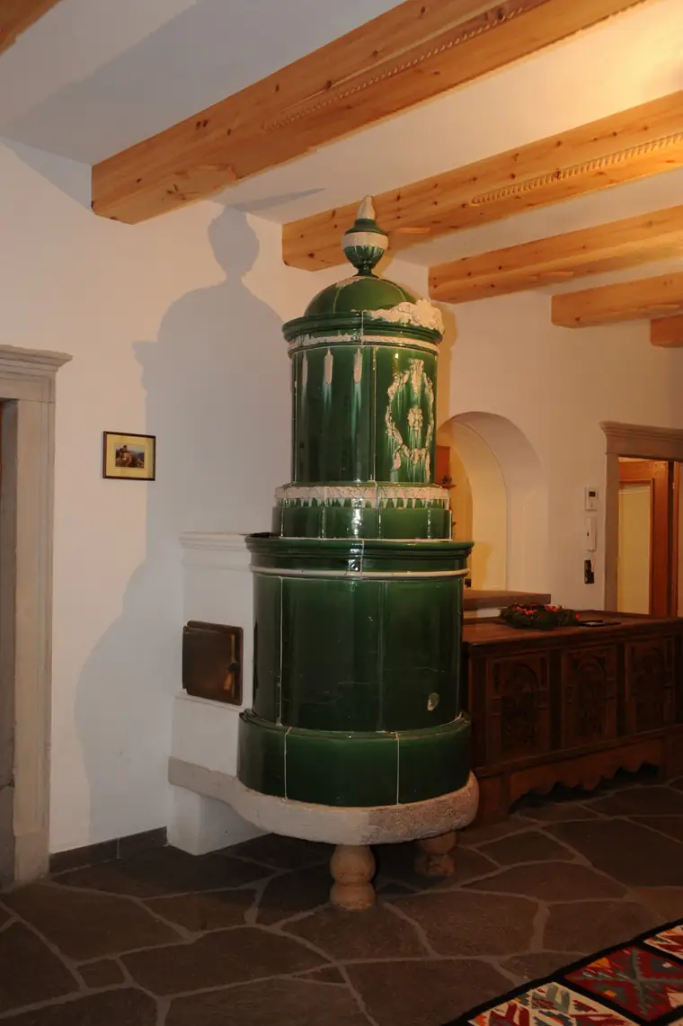 Grüner historischer Säulenofen unter einer Holzdecke