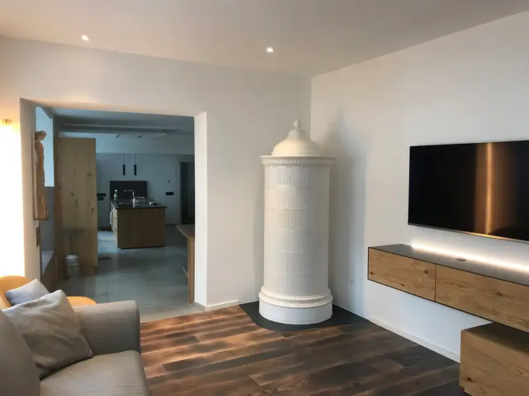 Weißer Säulenofen in einem modernen Wohnraum neben Sideboard und Fernseher